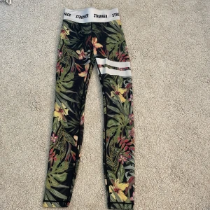 Blommiga leggings från Stronger XXS - Snygga leggings från Stronger i storlek XXS med tropiskt blommönster i grönt, gult och rosa. Hög midja med vit resår. Perfekt att träna i, dessa byxor är i väldigt bra skick 