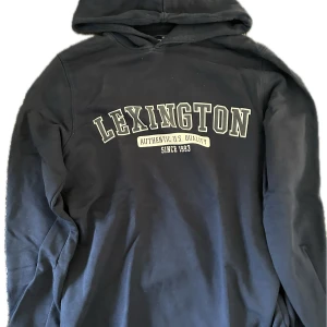 Lexington hoodie - Mörkblå hoodie från Lexington – en klassiker med premiumkänsla! Tillverkad i mjuk och tjock bomull med Lexington-logo framtill. Perfekt för både hemmamys och en avslappnad vardagslook. Tidlös färg som passar till allt. Inga fläckar eller skador – redo för ny användning!