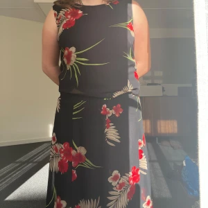 Svart blommigt set blus och långkjol vintage - Säljer en svart blus och långkjol med röda och vita blommor samt gröna blad. Klänningen är ärmlös och har en rak, avslappnad passform. Perfekt för sommardagar eller när du vill känna dig extra fin.