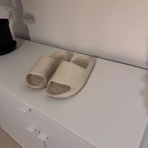 Beige yeezy slides  - Säljer ett par stilrena yeezy slides. De är tillverkade i syntetmaterial och har en minimalistisk design som passar perfekt för varma dagar.