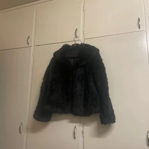 Svart pälsjacka med krage - Snygg svart pälsjacka med klassisk krage och lång ärm. Jackan har en fluffig och mjuk känsla, perfekt för att lyfta din outfit under kyliga dagar. Enkel att matcha och ger en lyxig vibe.