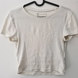 Vit croppad ribbad t-shirt från FSBN Sister - Säljer en vit croppad t-shirt från FSBN Sister. T-shirten är ribbad, har rund halsringning och korta ärmar. Perfekt till jeans eller kjol för en enkel och stilren look. Defekter finns: deofläckar i armhålorna, dova fläckar på hela tröjan och tyget har blivit tunnt vid bröstet. Fläckarna har jag inte försökt fläckbehandla.