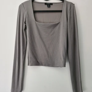 Grå långärmad topp från Amisu - Säljer en stilren grå långärmad topp från Amisu med fyrkantig ringning. Toppen är croppad och har en tight passform. Tillverkad i mjuk polyesterblandning med lite stretch för extra komfort. Noppror finns, men tas lätt bort med en noppmaskin.