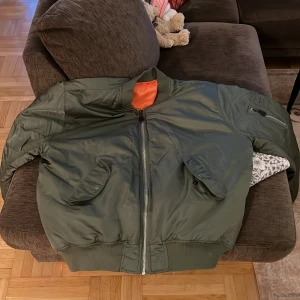 Olivgrön bomberjacka från Brandit 5XL - Säljer en olivgrön bomberjacka från Brandit i storlek 5XL. Jackan har orange foder, klassisk ribbad mudd i midja och ärmslut, två snedställda fickor med lock och dragkedja framtill. Tillverkad i nylon och polyester, perfekt för dig som gillar streetstyle.