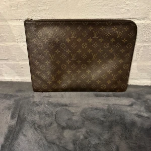 Louis Vuitton datafodral  - Säljer en klassisk brunt datafodral från Louis Vuitton med ikoniskt monogrammönster. Väskan är i skinn och har dragkedja upptill. Perfekt storlek för att bära det viktigaste och ger en lyxig touch till din outfit.