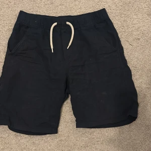 Svarta shorts med snörning från Lindex - Svarta shorts från Lindex med elastisk midja och vit snörning framtill. Modellen har två sidofickor och två bakfickor, perfekt för chill dagar. Materialet är mjukt och lätt, vilket gör dem sköna att bära under varma dagar. 