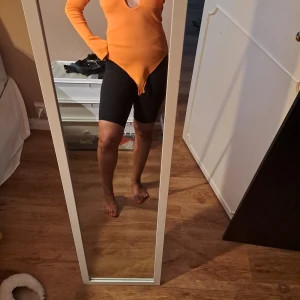 Orange långärmad bodysuit med cut out - Säljer en orange långärmad bodysuit med snygg cut out framtill och djup v-ringning. Tight passform som framhäver figuren och cool detalj med spetsig nederdel. Perfekt för dig som vill sticka ut med färg och form. Endast använd två gånger, normal i storleken.