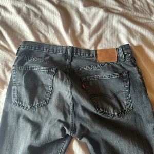Levi's 501 svarta jeans - Svarta Levi's 501 jeans med klassisk femficksdesign och knappgylf. Har ett litet hål vid skrevet men det är enkelt att bara sy igen om man nu vill det . 