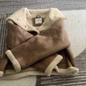 Beige teddyjacka från Zara - Säljer en snygg beige teddyjacka från Zara med mjukt foder och stora slag. Jackan har två fickor framtill, stängs med knapp och har en croppad passform. Perfekt för kalla dagar när du vill vara både varm och trendig.