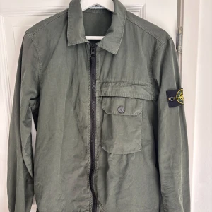 Stone Island Overshirt - Stone Island overshirt i militärgrön – stl S Säljer en snygg och stilren jacka från Stone Island i militärgrön färg. Klassisk design med dragkedja, bröstficka och den ikoniska Stone Island Patchen på vänstra ärmen. Passar perfekt för vår/sommar/höst. Använd fåtal gånger och har inga defekter.   Nypris: ca 5000kr