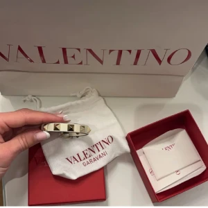 Valentino Garavani Rockstud armband - Snyggt Rockstud armband från Valentino Garavani i ljusbeige skinn med guldiga pyramidnitar. Justerbar storlek med spänne och ikonisk design som verkligen sticker ut. Perfekt accessoar för att lyfta din outfit. Pris kan absolut diskuteras!!❤️