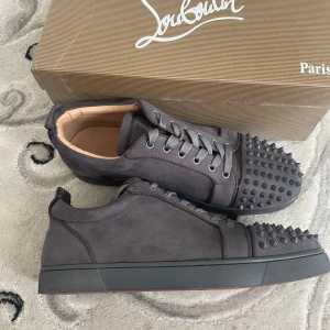 Christian Louboutin grå mocka sneakers - Snygga grå sneakers från Christian Louboutin i mocka med ikoniska röda sulor och coola nitar på tån. Skorna har snörning och en platt sula, perfekt för dig som vill sticka ut med en lyxig och edgy stil.