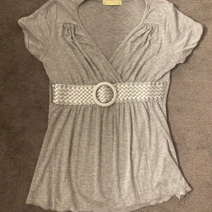 Grå omlottopp med flätat bälte - Grå omlottopp med korta ärmar och snygg v-ringning. Från nånstans under tidigt 2010-talet💕(köpare betalar frakten)