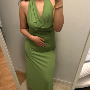 Grön långklänning med halterneck - Snygg grön långklänning med halterneck och draperad v-ringning. Klänningen är figurnära och har en mjuk, stretchig känsla som sitter skönt på kroppen. Perfekt för dig som vill sticka ut med en fräsch färg och elegant siluett.
