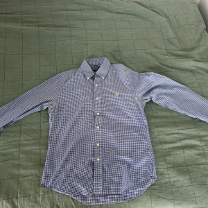 Blårutig skjorta Polo Ralph Lauren M - Snygg blårutig skjorta från Polo Ralph Lauren i slim fit-modell. Skjortan har klassisk krage, långa ärmar och knäppning framtill. Broderad gul logga på bröstet. Tillverkad i mjuk bomull som känns skön mot huden.