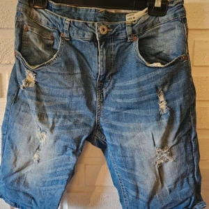  jeansshorts - Snygga blå jeansshorts från 157, modell Lorry. De har en klassisk femficksdesign, slitna detaljer och trasiga partier framtill för en cool, avslappnad look. Perfekta för varma dagar när du vill ha en streetig vibe.