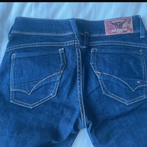 Tommy Hilfiger Jeans Lågmidjade - Mörkblå lågmidjadejeans från Tommy Hilfiger, modell Victoria Straight (omsydda till bootcut, nästan identisk färg på tyg så märks inte av😊). Klassisk femficksdesign med raka ben och snygga kontrastsömmar. Liten Hilfiger-flagga på fickan och rå, fransig fåll nedtill för en cool touch. Säljes då de tyvärr inte passar mig..