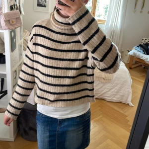 Randig polotröja från H&M i beige och svart - Supermysig ribbstickad polotröja från H&M i beige med svarta ränder. Tröjan har en loose fit, lång ärm och hög krage som ger en chill vibe. Perfekt till jeans eller kjol för en avslappnad look.