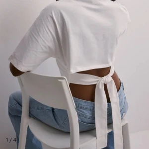 Vit omlottopp med knyt i ryggen - Säljer en vit croppad topp i bomull med korta ärmar och snygg öppen rygg. Toppen har breda knytband som knyts i ryggen för en cool och trendig look. Perfekt till jeans eller kjol för en stilren vibe.