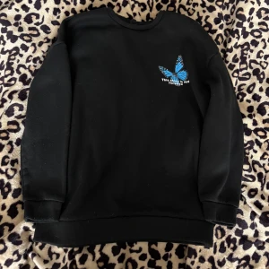 Svart sweatshirt med tryck - Svart sweatshirt med tryck av en blå fjäril samt texten 'This story is not finished' både fram och bak. Tröjan har långa ärmar och är gjord i fleecetygs håller. Den är xs och är oversized
