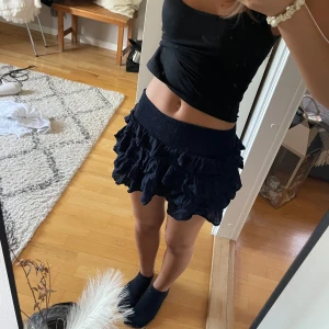 Mörkblå volangkjol från Subdued - Supersöt mörkblå kortkjol från Subdued med bred, smockad midja och flera lager volanger. Kjolen är lätt och luftig, perfekt för en trendig look. Materialet känns mjukt och bekvämt mot huden. Säljes med originaltag kvar.