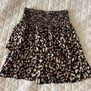 Leopardmönstrad kortkjol från Pigalle - Supersnygg kortkjol från Pigalle med leopardmönster i svart, beige och brunt. Kjolen har smock i midjan och volanger. Det står inte storlek men passar mig som har storlek XS eller 158/164 i kjolar. Pris går att diskutera🥰