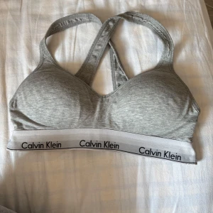 Grå sportig linnetopp Calvin Klein M - Säljer en grå sportig linnetopp från Calvin Klein med brottarrygg och bred resår med logga. Mjuk och stretchig blandning av bomull, modal och elastan. Perfekt för chill eller träning, med bekväm passform och stilren look. Använd varsamt så inge defekter eller liknande. Stl M. Säljes för 150kr. Bara att höra av dig!🥰