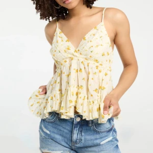 Blommig volangtop med smala axelband - Supersöt blommig linnetopp i ljusgul med små gula blommor och volangkant. Djup v-ringning och tunna axelband ger en luftig känsla. Perfekt för varma dagar när du vill ha en romantisk och chill vibe.