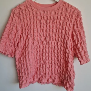 Rosa bubblig topp med kort ärm - Superfin rosa topp med korta ärmar och unik bubblig struktur i tyget. Den var blivit noppig på delar av plagget