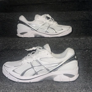 ASICS GT-2160 - Snygga vita ASICS GT-2160 sneakers med silvriga detaljer och meshpaneler för extra andningsförmåga. Skorna har snörning, rund tå och en chunky sula i syntetmaterial. Perfekta för dig som gillar sportig och clean stil.