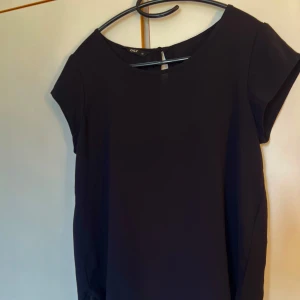 Svart blus från ONLY - Enkel och stilren svart blus från ONLY i storlek 34. Blusen har rund halsringning, korta ärmar och en lätt, flowy passform. Nederkanten har en diskret vågig detalj som ger en söt touch. Perfekt för dig som gillar minimalistisk stil.