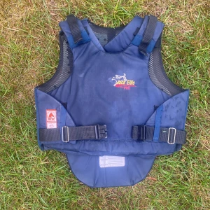 Jack Ellis blå skyddsväst för ridning - Mörkblå skyddsväst från Jack Ellis med justerbara axel- och midjeband, meshpaneler på sidorna och broderad logga framtill. Västen är certifierad enligt BETA-standard och passar perfekt för ridning. Kan även göras kortare vid ryggen. Säljs inte längre. Pris kan diskuteras.