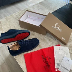 Mörkblå sneakers från Louboutin - Snygga mörkblå sneakers från Christian Louboutin i mocka med ikonisk röd sula. Skorna har rund tå, platt sula och klassisk snörning. Perfekta för dig som vill sticka ut med exklusiv design och lyxiga detaljer.