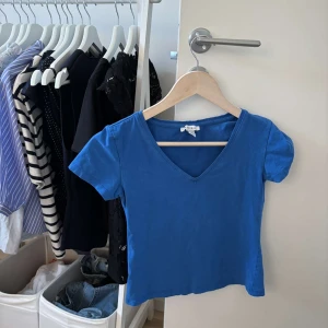 Blå v-ringad topp  - En enkel och stilren blå topp med v-ringning och korta ärmar. Modellen är croppad och passar perfekt till jeans eller kjol. Tillverkad i mjuk bomull som känns skön mot huden.