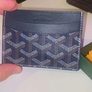  korthållare i mörkblått skinn - Säljer en snygg korthållare  i mörkblått skinn med deras ikoniska mönster i vitt och brunt. Slimmad design med flera kortfack, perfekt för dig som vill ha stilren och lyxig accessoar i fickan. Kommer med original ask och tygpåse.