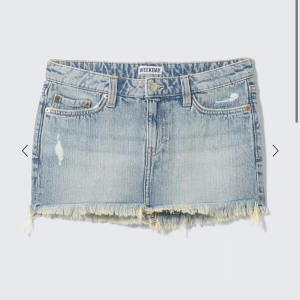 Ljusblå jeanskjol från Weekday - Säljer en ljusblå jeanskjol från Weekday med råa, fransiga kanter och slitna detaljer. Kjolen har klassisk femficksdesign, låg midja och knappgylf. Perfekt för dig som gillar en avslappnad och trendig stil.
