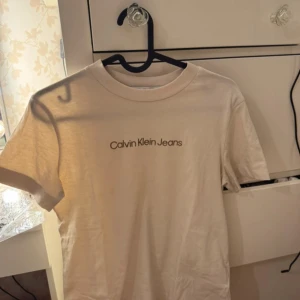 Beige t-shirt Calvin Klein Jeans XS - Snygg beige t-shirt från Calvin Klein Jeans i 100% bomull. Klassisk rund halsringning och korta ärmar. Framsidan har en stilren logga. Perfekt basic-plagg med relaxed vibe och enkel passform.