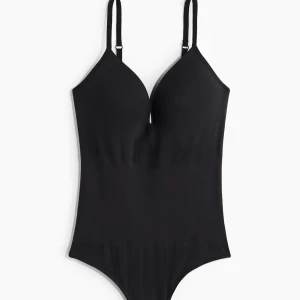 Den svarta populära bodyn med v-ringning - Snygg svart body med djup v-ringning och smala, justerbara axelband. Stilren och enkel design som sitter tight mot kroppen och framhäver figuren. Säljer då den var för stor för mig och endast använd två gånger så bra skick.