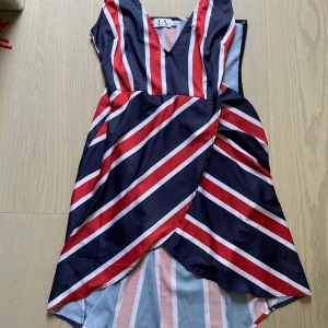 Randig kortklänning Linn Ahlborg x NA-KD - Superfin kortklänning med v-ringning från Linn Ahlborg x NA-KD. Klänningen har ett randigt mönster i marinblått, rött och vitt, omlott framtill och är ärmlös. Perfekt för dig som gillar färg och vill sticka ut lite extra.