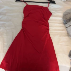 Röd kort klänning från H&M  - Snygg röd klänning från H&M Divided i kort modell med smala axelband. Klänningen har en enkel, figurnära passform och lätt rynkade detaljer i sidan. Perfekt för dig som gillar en stilren look med färg.