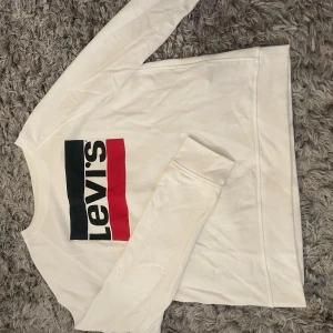 Vit långärmad tröja från Levi's - Vit långärmad tröja från Levi's med klassisk logga i svart, vitt och rött framtill. Tröjan har rund halsringning och är tillverkad i mjuk bomull. Perfekt för en avslappnad och stilren look. I storlek M men den är liten i storlek så skulle säga XS/S. Den är använd fåtal gånger och ser nästan ny ut!🤍