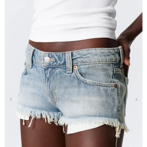 Lågmidjade jeansshorts med fransig kant - Snygga lågmidjade jeansshorts i ljusblå denim med slitna detaljer och fransig rå kant. Klassisk femficksmodell med bälteshällor och knappgylf. Perfekta för varma dagar och en avslappnad look. Köpta här på plick står ingen storlek i dem men hon sa att de va m men jag skulle säga att de är stora i storleken där av säljer ja de för de va alldeles förstora för mig.