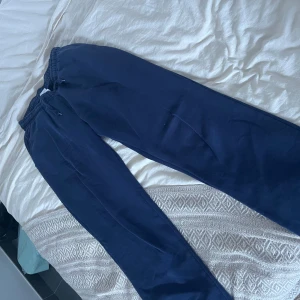 Mörkblå mjukisbyxor från Gina Tricot  - Mörkblå mjukisbyxor med resår och snörning i midjan. Byxorna har en loose passform och är tillverkade i mjukt bomullsmaterial. Perfekta för chill dagar eller när du vill vara extra bekväm. Finns ett litet fläck av klor på baksidan 