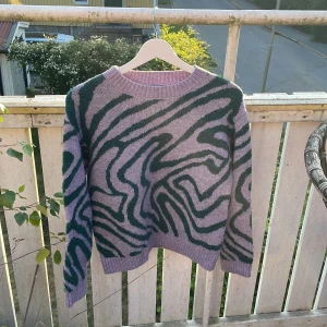 Lila stickad tröja med zebramönster Lindex - Cool stickad tröja från Lindex i lila med grönt zebramönster. Tröjan har rund hals, ribbade muddar och är långärmad. Perfekt för dig som vill sticka ut med ett unikt mönster och mjukt material.