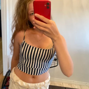 Randig croppad linnetopp med knyt - Säljer en croppad linnetopp med marinblå och vita ränder. Toppen har smala axelband och knyt i ryggen för en snygg passform. Perfekt för varma dagar och ger en fräsch sommarkänsla.