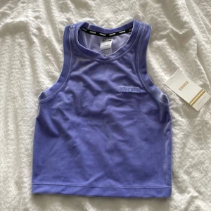 Lila croppad linnetopp från Stronger - Säljer en croppad linnetopp från Stronger i snygg lila nyans. Toppen har broderad logga framtill och är tillverkad i mjuk polyesterblandning med lite stretch. Perfekt för träning eller när du vill ha en sportig vibe.