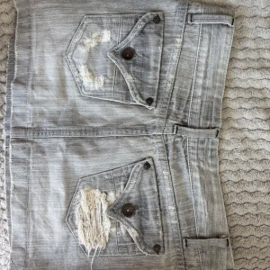 Grå jeanskjol med slitningar - Säljer en grå jeanskjol i kort modell med coola slitningar och gråa detaljer. 