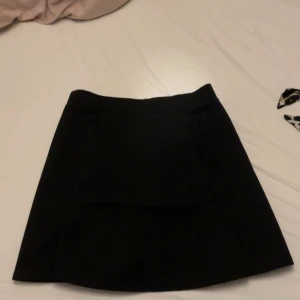 Svart ribbad kortkjol från H&M Divided - Svart ribbad kortkjol från H&M Divided i storlek M. Kjolen har en stilren design med dragkedja bak och är tillverkad i ett stretchigt material som sitter snyggt på kroppen. Perfekt att matcha med en crop top eller oversized hoodie.