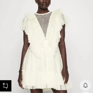 Klänning ida Sjöstedt - Superfin vit kortklänning med volanger och pärldetaljer. Klänningen har v-ringning, transparent mesh upptill och ärmlös design. Den är dekorerad med små pärlor och har en romantisk, fluffig look med lager av tyll. Perfekt för student eller sommarens alla tillfällen. Endast använd 1 gång.