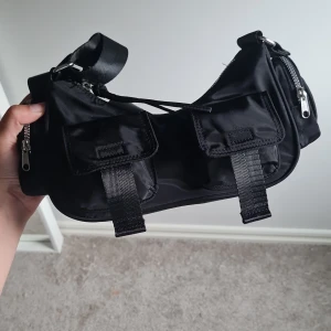 Svart axelväska från H&M Divided - Helt ny väska från H&M. Prislappen och allt papper inuti är kvar. Säljer då jag fick i väskan i present för ett tag sen men har inte använt den.